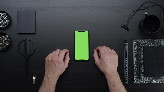 Male hands using smart device with green screen chroma on black clean minimalistic table with top view