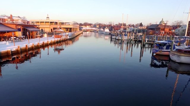 Medium aerial shot moving down Ego Alley in historic Annapolis Maryland during a golden winter sunrise. Snow on the boats.