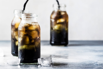 Healthy food and drink concept: cold black detox mineral water with crushed ice in glass bottles, with activated charcoal, gray stone table background, trendy beverage, copy space, selective focus