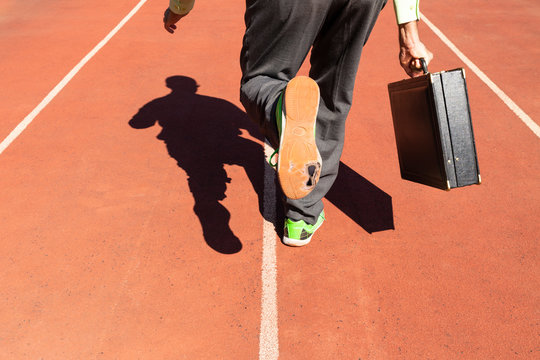 A business man in gray suit with green shirt, black briefcase and broken green sports shoes running on a running track