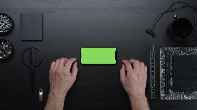 Male hands using smart device with green screen chroma on black clean minimalistic table with top view