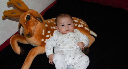 cute tre months old baby boy dressed in white on black blanket and dear soft toy