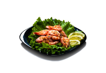 Boiled shrimps with lemon slices on a sheet of lettuce on a black plate isolated on white background.