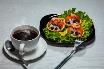 Sample breakfast consisting of a snack with red fish and a cup of hot coffee on a wooden table.
