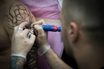 Tattoo artist in gloves paint on a man’s shoulder