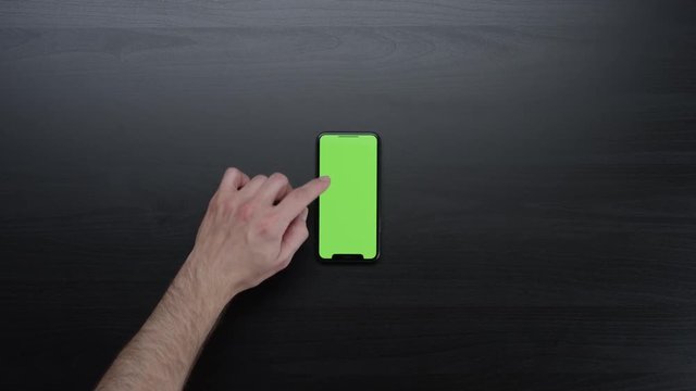 Male hands using smart device with green screen chroma on black clean minimalistic table with top view