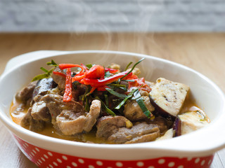 Delicious homemade spice Thai food with vegetables, pork and chicken spicy red curry in a red dots deep plate on wooden table.