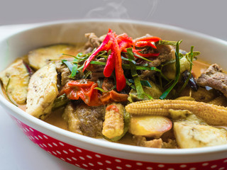 Delicious homemade spice Thai food with vegetables, pork and chicken spicy red curry in a red dots deep plate on wooden table.