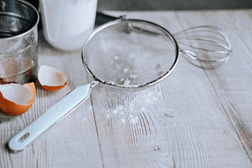 Kitchen utensils for making pancakes, egg shells and scattered flour on a wooden kitchen table