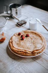 Breakfast with russian bliny or thin sweet crepes, jam, berries and yogurt on a rustic wooden table in daylight