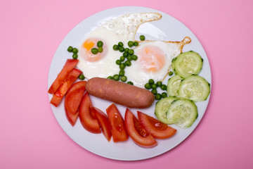 Homemade fried eggs with sausages on a white plate on a pink background. Classic breakfast. View from above.