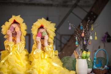 Twin sisters at Easter eat ginger cookies, painted eggs, laugh. Girls in the kitchen in costumes chicken.
