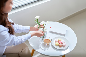 Woman arranging lisianthus flowers in a glass vase at home.