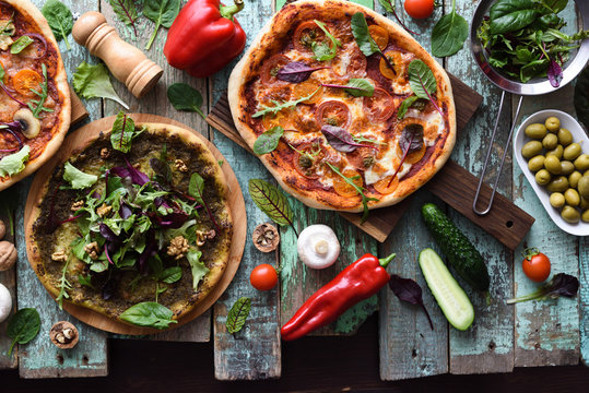 Flatlay of vegetarian pizzas with raw ingredients. Green pesto pizza, tomato and mushrooms pizza on shabby blue background