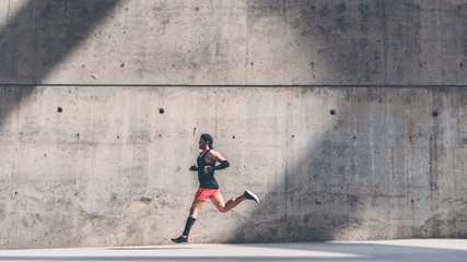 Muscular man athlete sprinter running fast,exercising outdoors,jogging outside against gray concret background with copy space area for text message or ad content.Side view,full length