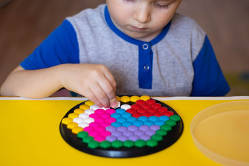 Fototapeta premium A little boy lays out a multicolored mosaic. Child playing at the table