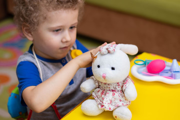 Fototapeta na wymiar Little boy plays doctor, treats a teddy bunny