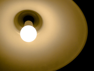 Simple light bulb in a lamp with warm light and black dark background,