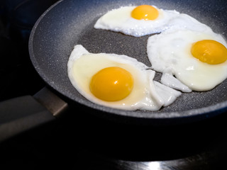 Fried eggs in a stone surface pan with handle on black stove.