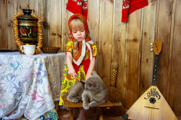 a little girl in russian folk clothes at the celebration of the slavic holiday of maslenitsa plays with a cat