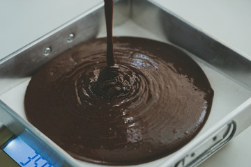 Dark brown chocolate cream is poured on a tray for baking in a heat oven. This cream is the raw material for this bakery brownie. The image is vintage tone.