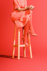 cropped view of elegant girl posing in living coral dress on stool on red background