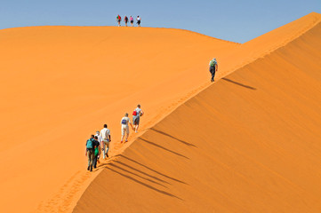 Tourists walking up a red dune in Sossuslvei, Namib Naukluft National Park, Namib desert, Namibia.