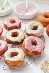 Homemade donuts decorated with colored icing and colored sugar on a light background.