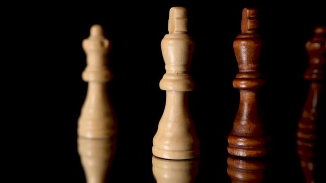 Brown and whit king, and brown and white queen, chess figures standing against each oter.