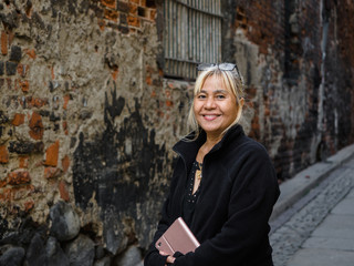60 years old age Asian Thai woman with technology smart tablet, mobile phone, and glasses on her head traveling in Europe old beautiful city view on background for holiday.