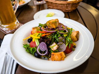 Grilled salmon salad with greens, onion, vegetables, tomato. Italian cuisine. Top side view on wooden background with a glass of beer in a restaurant.