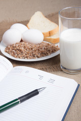 Notebook with buckwheat,bread,eggs and a glass of milk