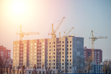 Under construction high-rise building with yellow construction crane in the sunlight