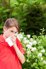 Teen boy blowing his nose on a tissue in a spring garden seasonal infection concept