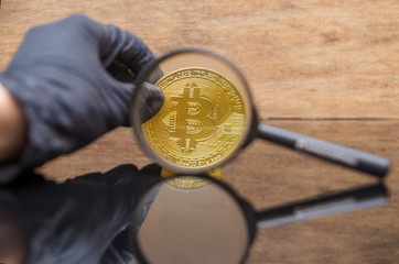 hand holding magnifying glass looking on new virtual money btc bitcoin with reflection. Crypto...