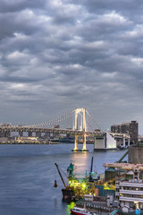 Obraz premium Rainbow Bridge with Cargo and cruise ships moored or sailing in Odaiba Bay of Tokyo.
