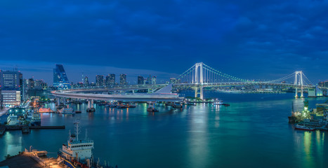 Panorama of the circular highway leading to the Rainbow Bridge with Cargo and cruise ships moored or sailing in Odaiba Bay of Tokyo.