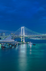 Fototapeta na wymiar Circular highway leading to the illuminated Rainbow Bridge with cruise ships moored in Odaiba Bay of Tokyo.