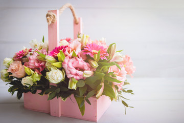 Flower arrangement bouquet of rose, alstroemeria, gerbera, in a pink basket on a gray wooden background.