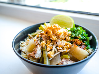 Shred chicken instant noodles with deep fried garlic. chili powder, lemon, spring onion and hot soup with spices in a bowl on white table, Thai noodles food
