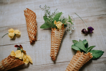 Waffle cones with bouquets of spring flowers and green herbs inside on a wooden rustic background. Soft selective lens focus.