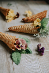 Waffle cones with bouquets of spring flowers and green herbs inside on a wooden rustic background. Soft selective lens focus.