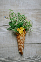 Waffle cone with spring flowers and green leaves inside