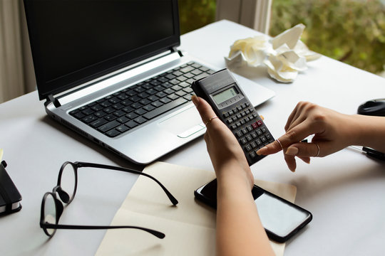 The hands of a young woman hold a calculator in front of a laptop in the office. a female accountant calculates on a calculator. The student works for a final exam in mathematics, physics, chemistry.