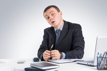 Serious businessman skeptically looking at you sitting at his desk on gray background.Human face expression