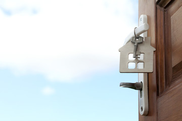 welcome to stay. open door to the street with a key and a key fob in the shape of a house symbol with a view of the cloud in the sky