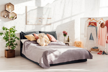modern interior design of bedroom with teddy bear toys, pillows, clothes on racks and bed
