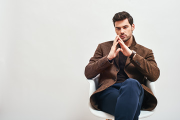 Waiting for interview. Stylish dark-haired man sitting on a chair, crossing his legs and looking at...