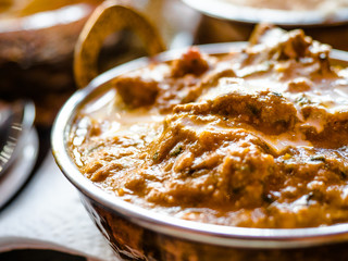 Indian Food or Indian Curry in a copper brass serving oriental bowl, pieces of chicken fillet in curry sauce ingredients in a pan with the old table side view close-up, Set of Indian food.