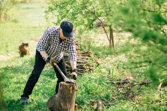 Senior man in baseball cap with axe chopping wood. Elderly arborist man working in garden. Active retirement lifestyle concept.